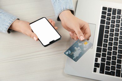 Online payment. Woman using credit card and smartphone with blank screen near laptop at white wooden table, above view