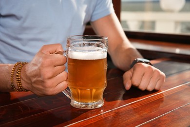 Photo of Man with glass of tasty beer at wooden table in pub, closeup