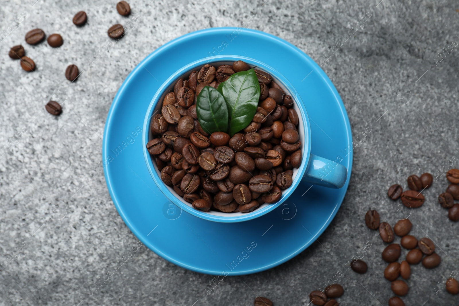 Photo of Cup with roasted coffee beans and leaves on grey table, flat lay