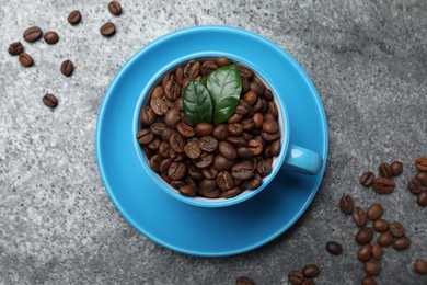 Photo of Cup with roasted coffee beans and leaves on grey table, flat lay