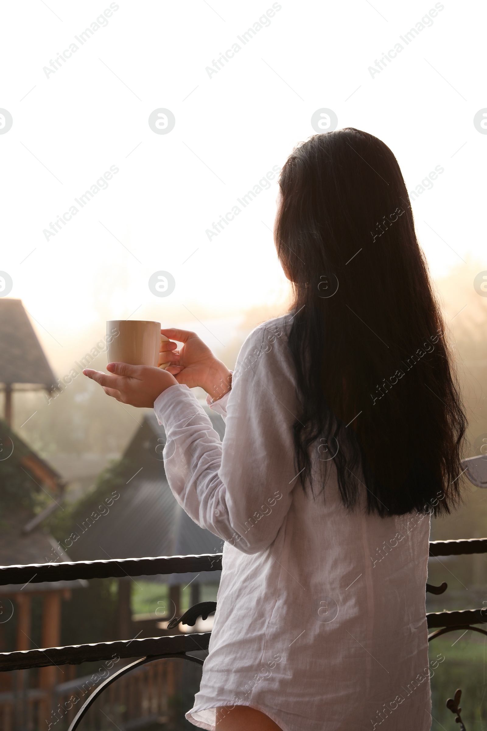 Photo of Young woman with cup of tea standing on balcony in morning