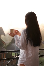 Young woman with cup of tea standing on balcony in morning