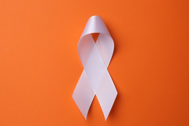 Photo of White awareness ribbon on orange background, top view
