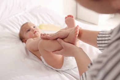 Photo of Mother massaging her cute baby with oil on bed at home, closeup