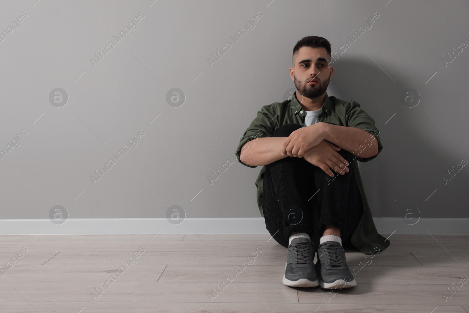 Photo of Sad man sitting on floor near light grey wall. Space for text