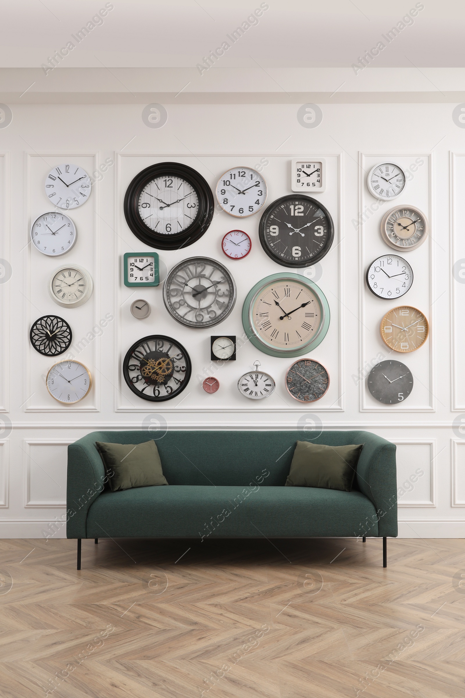 Photo of Collection of different clocks and comfortable sofa in stylish room. Interior design