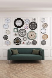 Photo of Collection of different clocks and comfortable sofa in stylish room. Interior design