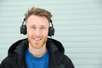 Photo of Young man listening to music with headphones against light wall. Space for text