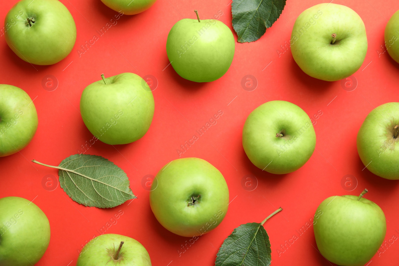 Photo of Fresh ripe green apples and leaves on red background, flat lay