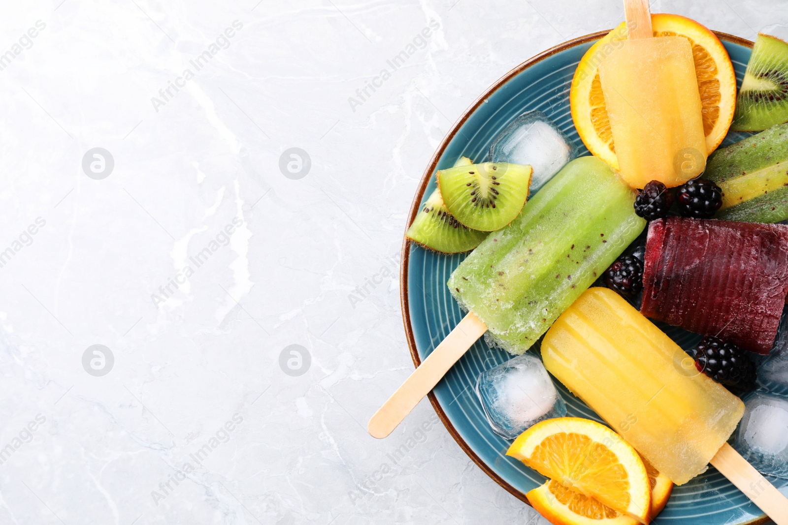Photo of Plate of delicious popsicles, ice cubes and fresh fruits on light grey marble table, top view. Space for text