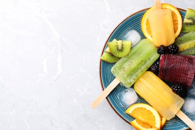 Photo of Plate of delicious popsicles, ice cubes and fresh fruits on light grey marble table, top view. Space for text