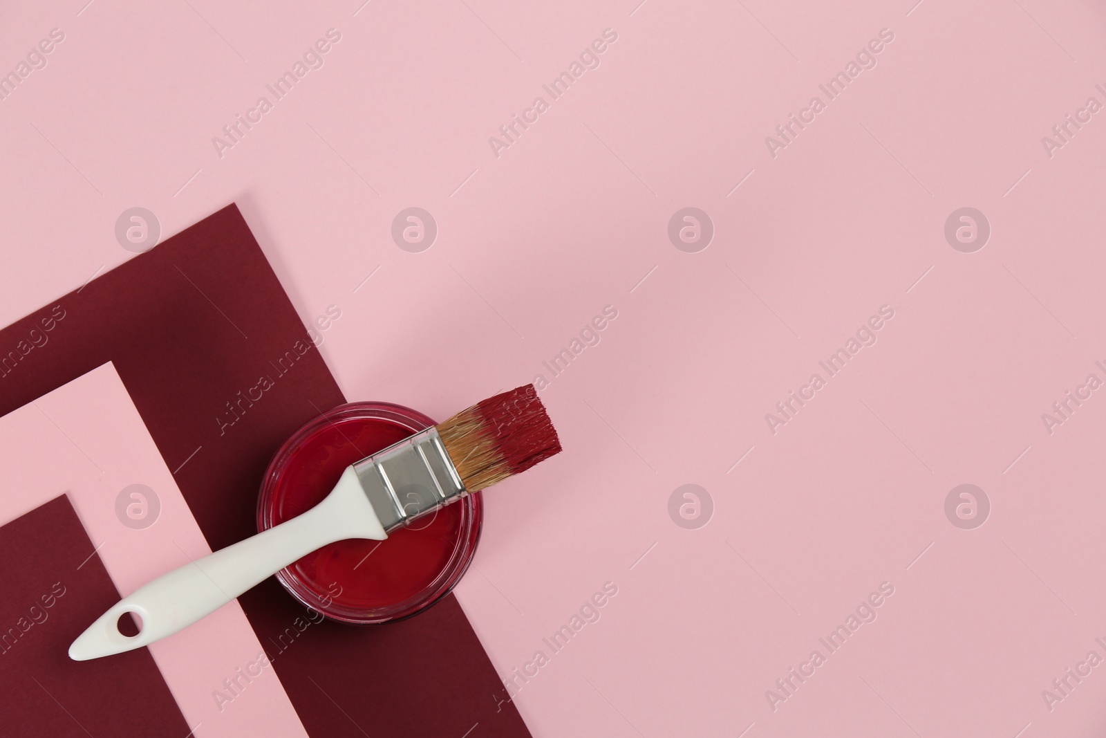 Photo of Can of burgundy paint with brush on color background, top view. Space for text