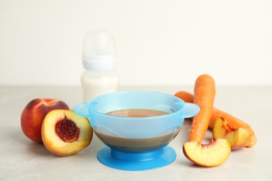 Baby food in bowl and fresh ingredients on light grey table