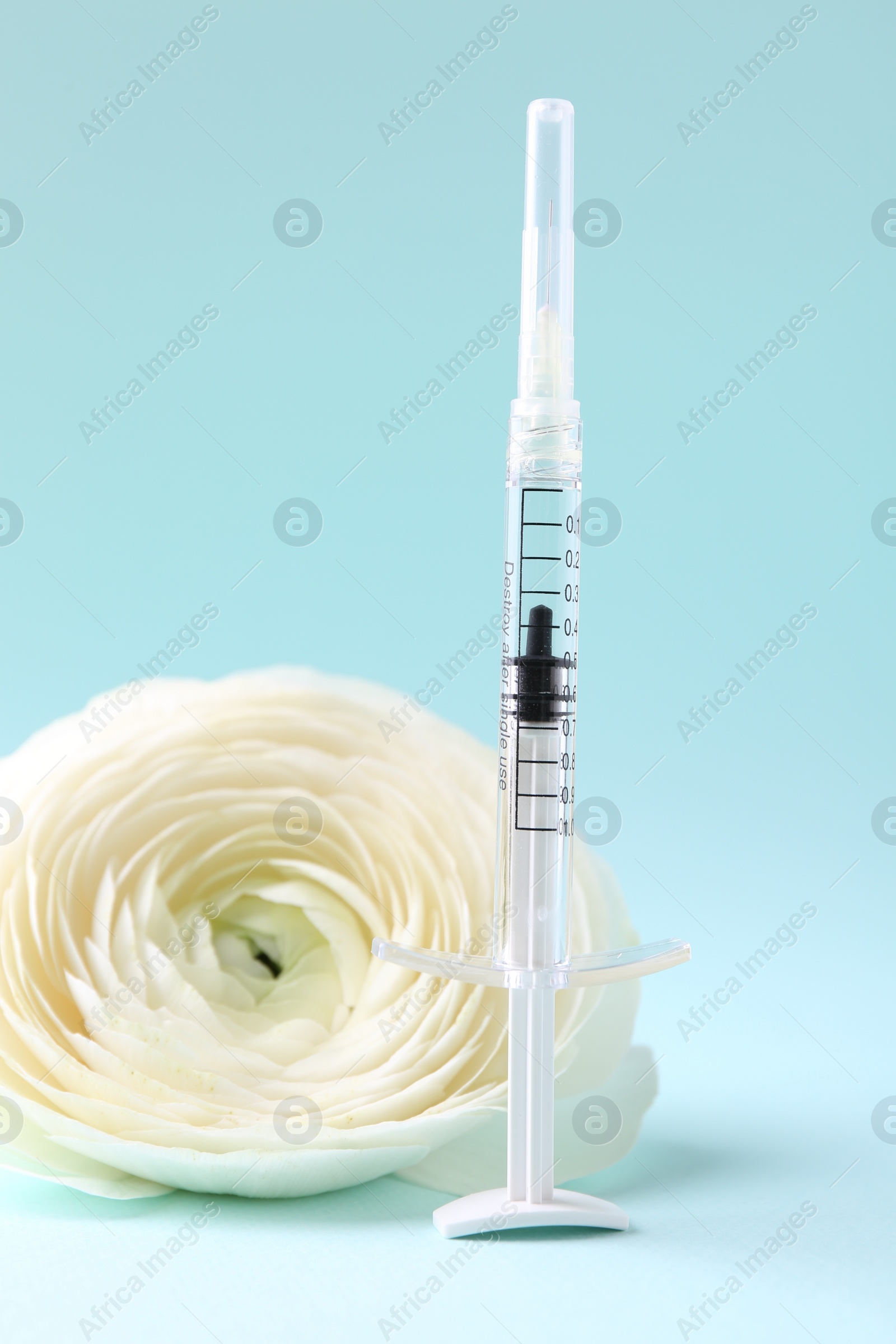 Photo of Cosmetology. Medical syringe and ranunculus flower on light blue background