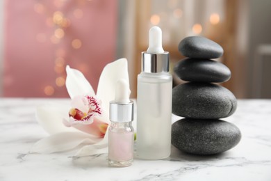 Photo of Essential oil, spa stones and orchid flower on white marble table against blurred lights