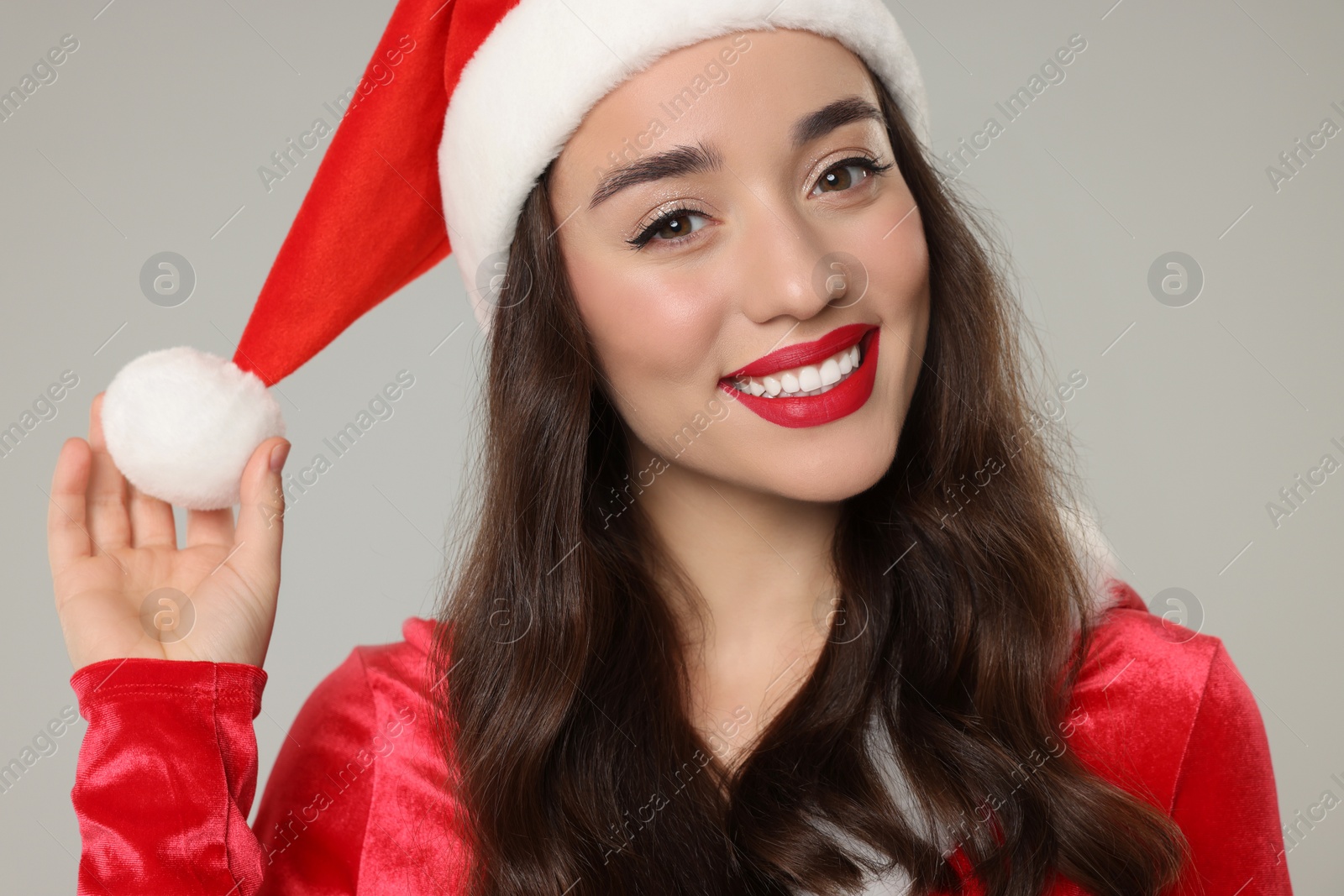 Photo of Christmas celebration. Beautiful young woman in Santa hat on grey background, closeup