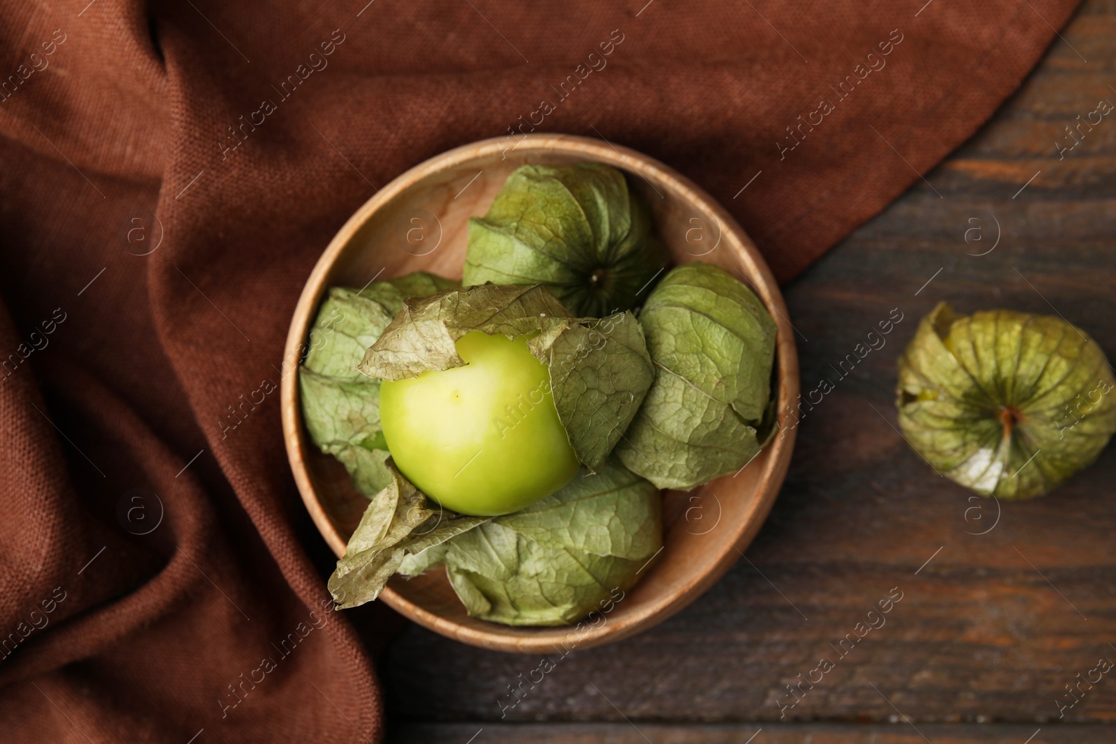Photo of Fresh green tomatillos with husk in bowl on wooden table, top view