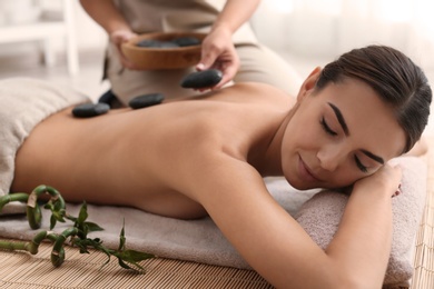 Beautiful young woman getting hot stone massage in spa salon