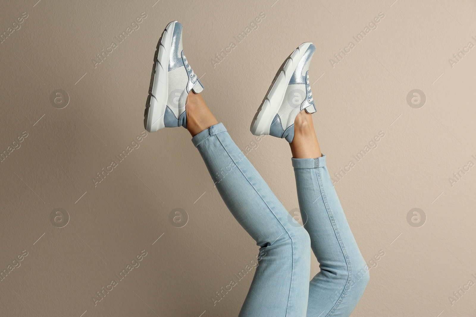 Photo of Woman wearing sneakers on beige background, closeup