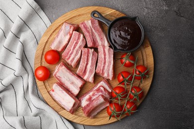 Photo of Cut raw pork ribs, tomatoes and sauce on grey table, top view