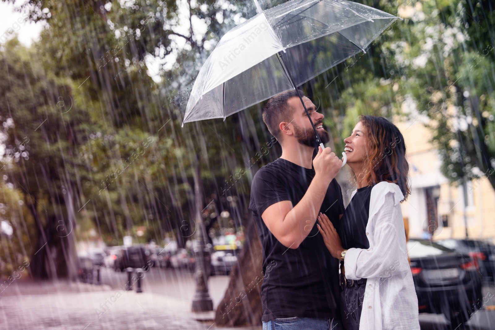 Image of Young couple with umbrella enjoying time together under rain on city street