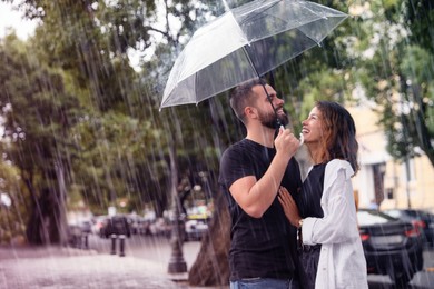 Young couple with umbrella enjoying time together under rain on city street