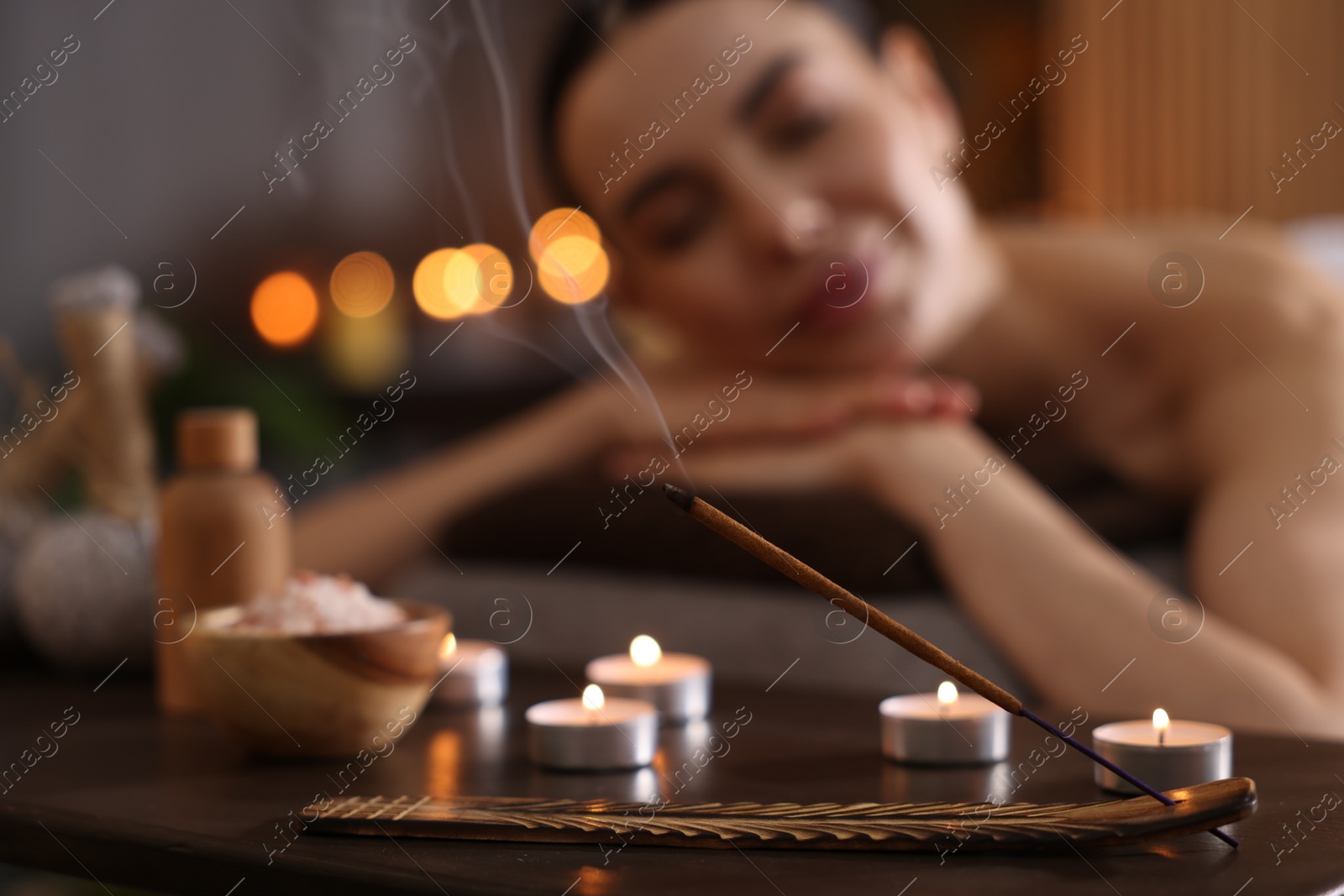 Photo of Spa therapy. Beautiful young woman lying on massage table in salon, focus on burning candles, salt and incense stick