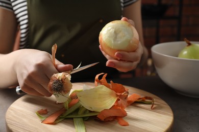 Photo of Woman peeling fresh onion at table indoors, closeup