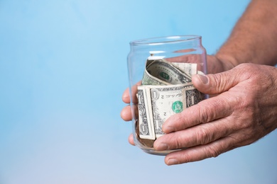 Photo of Man holding donation jar with money on color background, closeup. Space for text