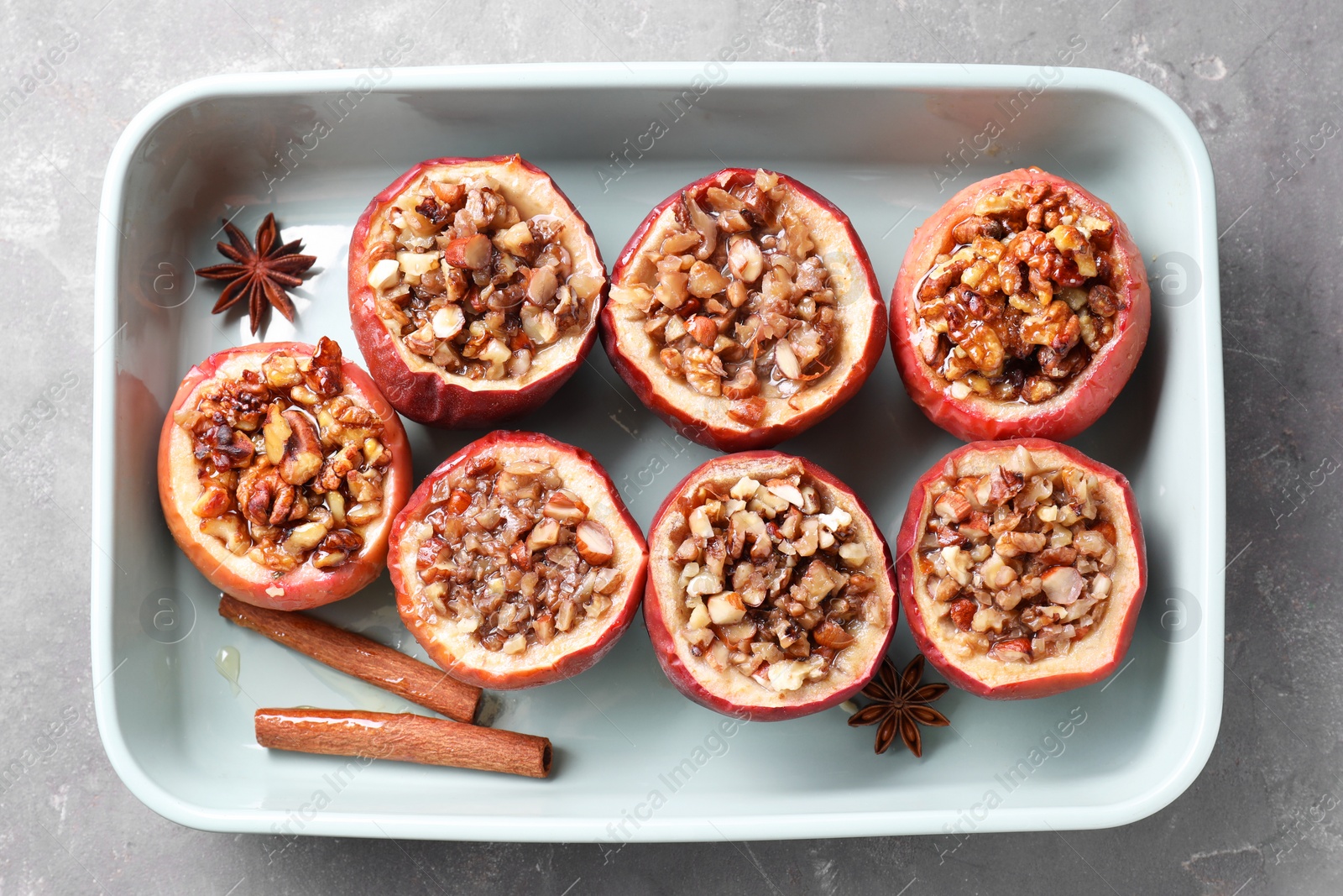 Photo of Tasty baked apples with nuts, honey and spices in dish on gray table, top view