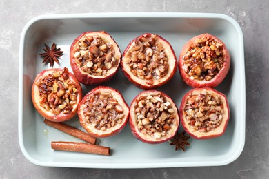 Tasty baked apples with nuts, honey and spices in dish on gray table, top view