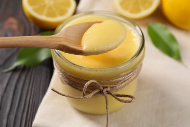 Photo of Taking delicious lemon curd from glass jar at wooden table, closeup