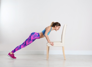 Photo of Young woman exercising with chair near white wall. Home fitness