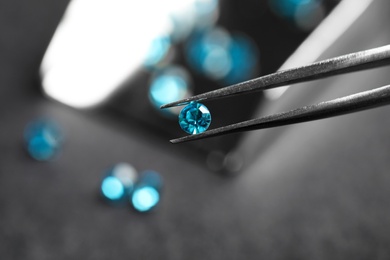 Photo of Tweezers with beautiful gemstone on blurred background