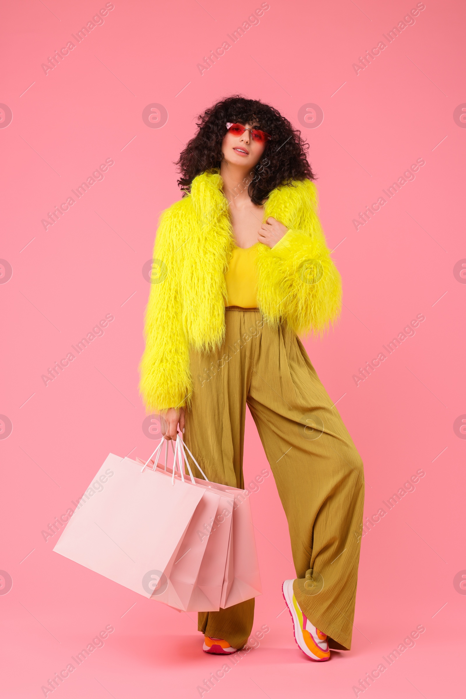 Photo of Happy young woman with shopping bags on pink background