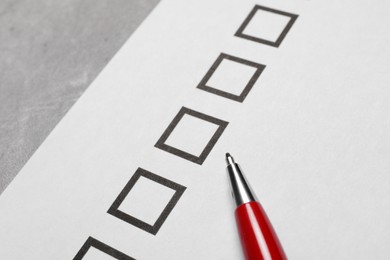 Paper sheet with checkboxes and pen on light grey table, closeup. Checklist