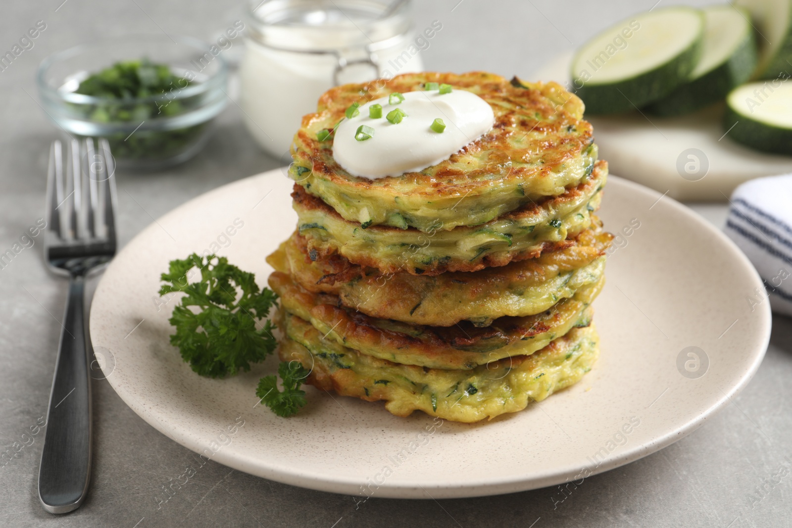 Photo of Delicious zucchini fritters with sour cream on grey table