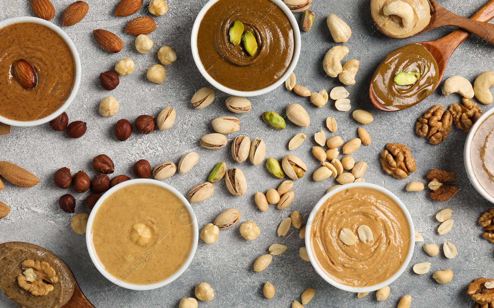 Photo of Tasty nut butters and raw nuts on light grey table, flat lay