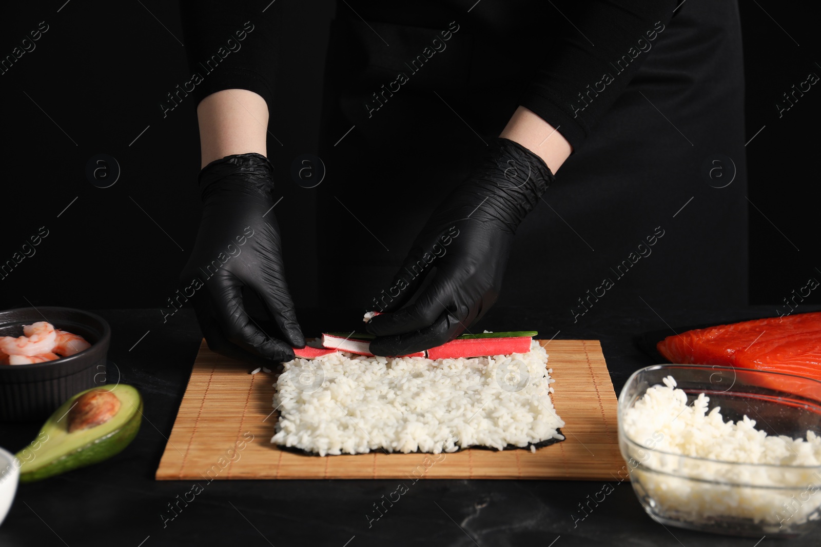 Photo of Chef in gloves making sushi roll at dark table, closeup