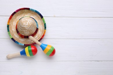 Photo of Colorful maracas and sombrero hat on white wooden table, flat lay with space for text. Musical instrument