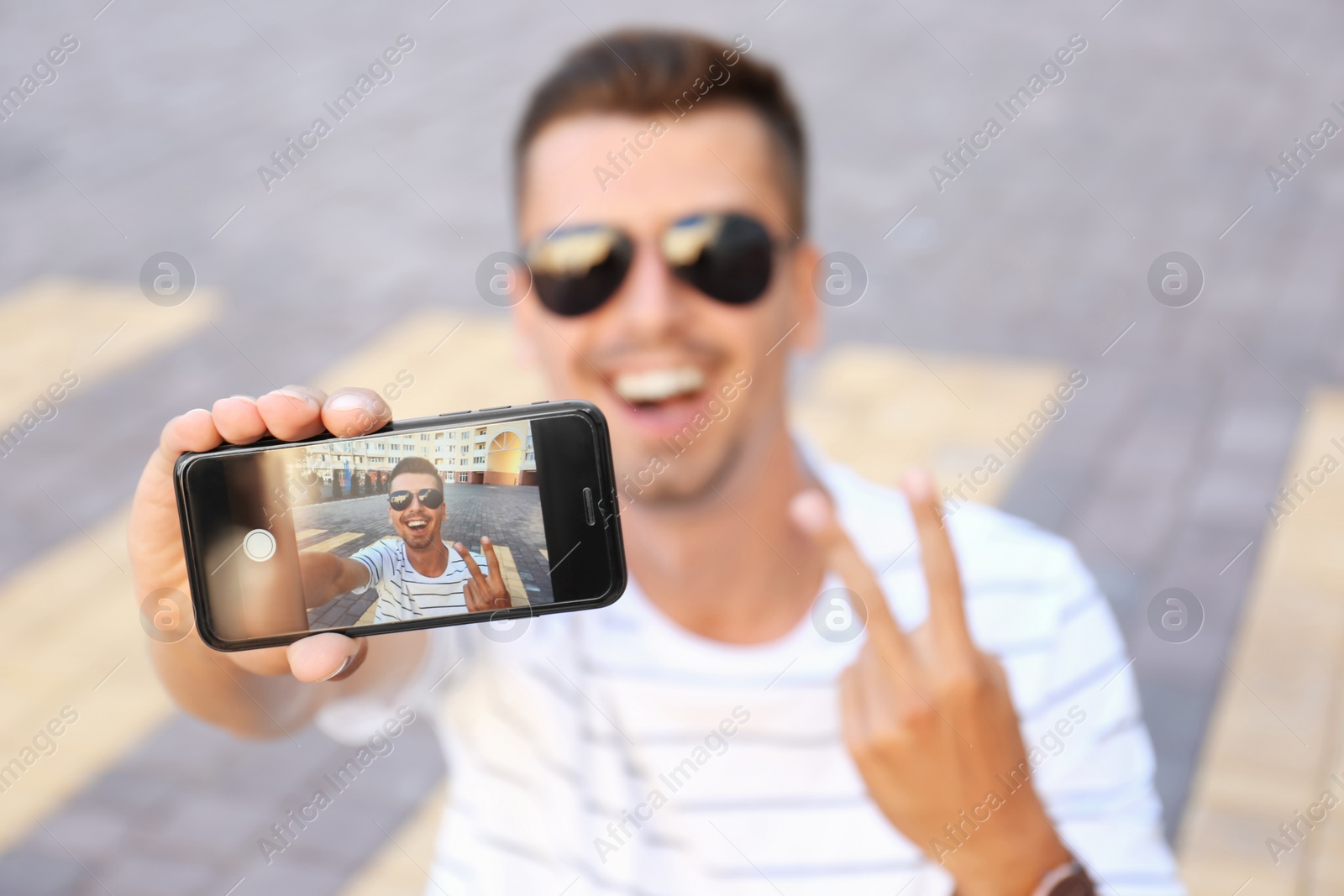 Photo of Young man taking selfie outdoors, focus on smartphone