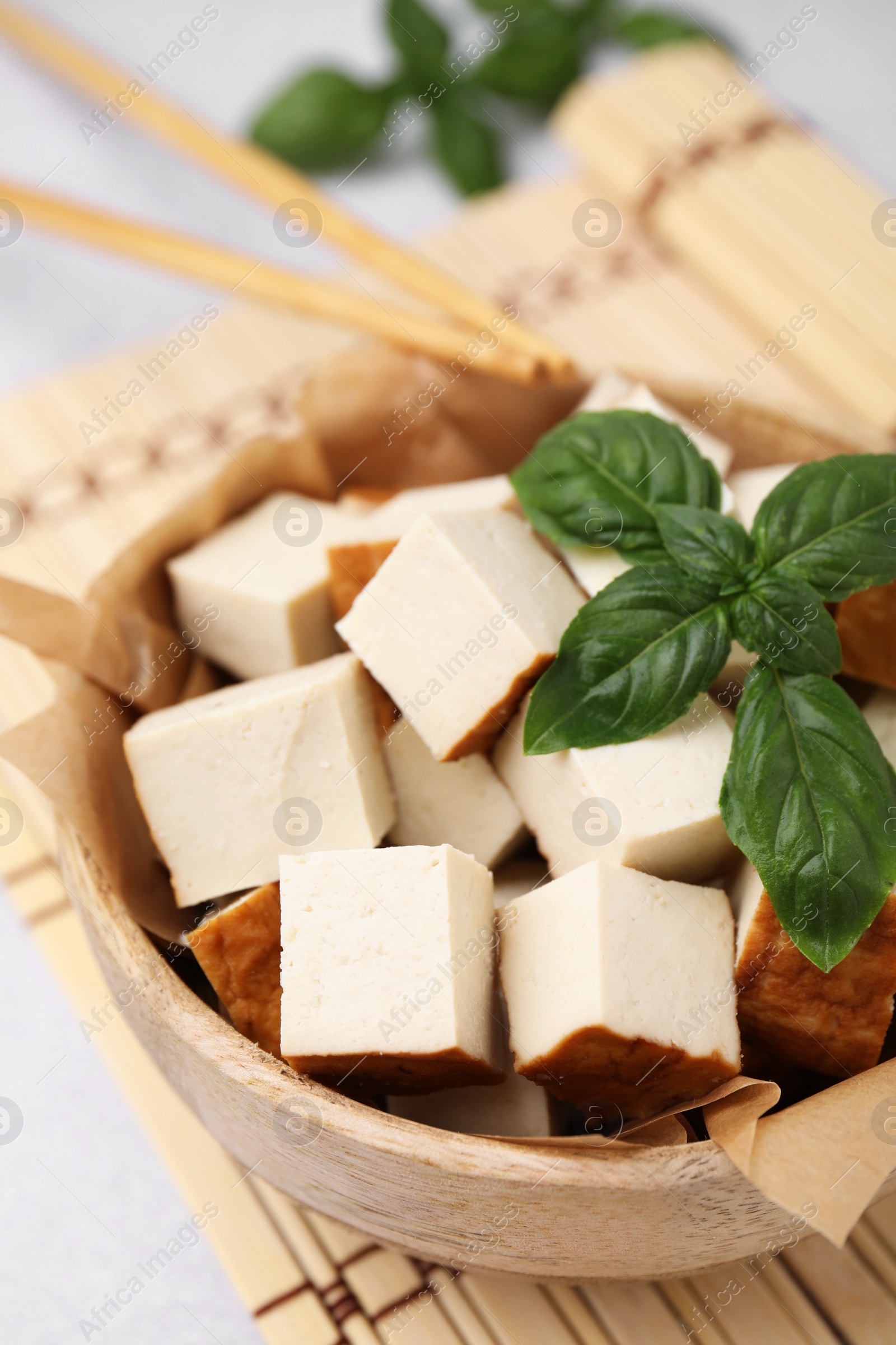 Photo of Bowl of smoked tofu cubes and basil on white table, closeup