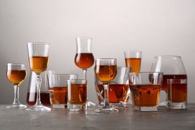 Photo of Different delicious liqueurs in glasses on grey table