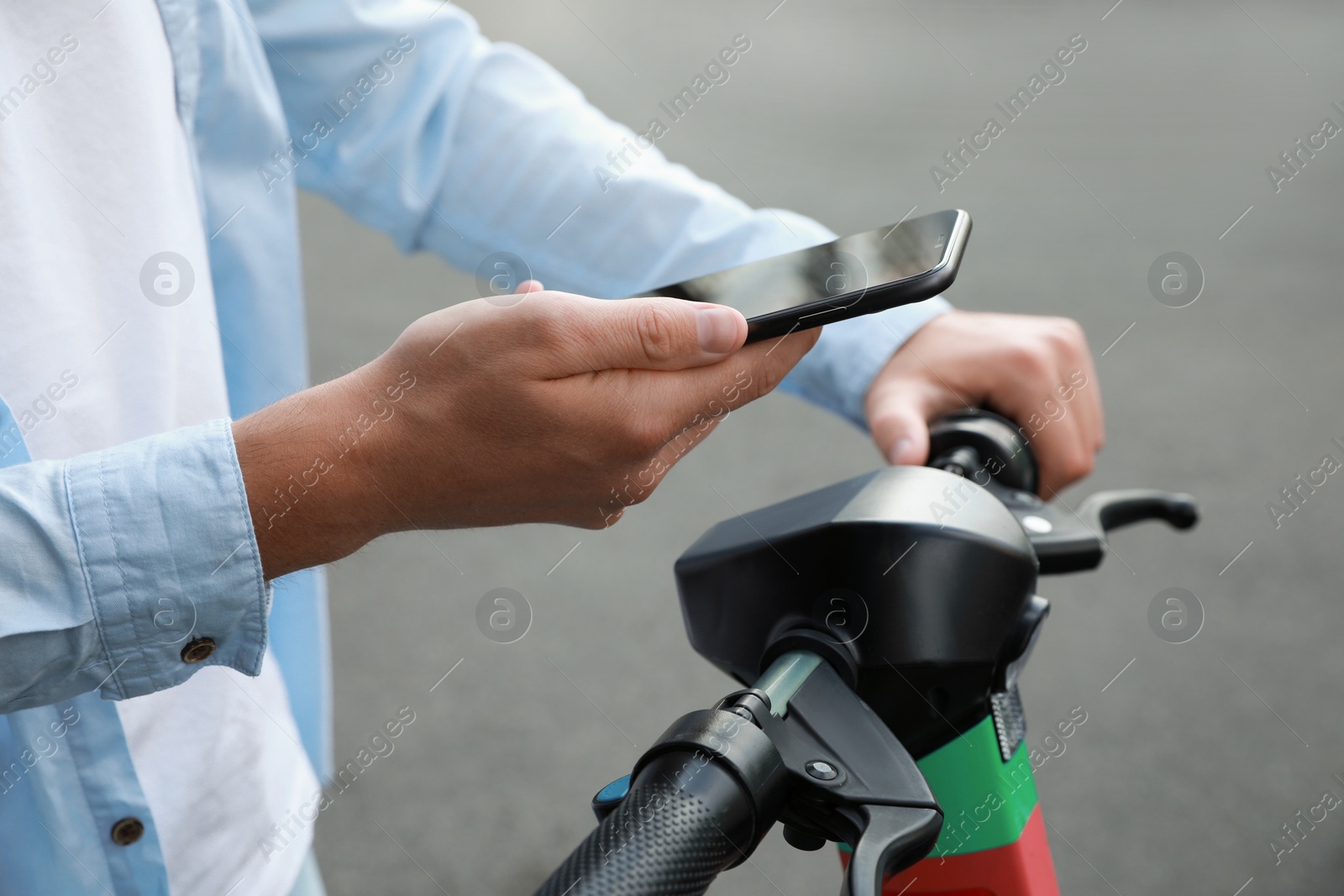 Photo of Man using smartphone to pay and unblock electric kick scooter outdoors, closeup