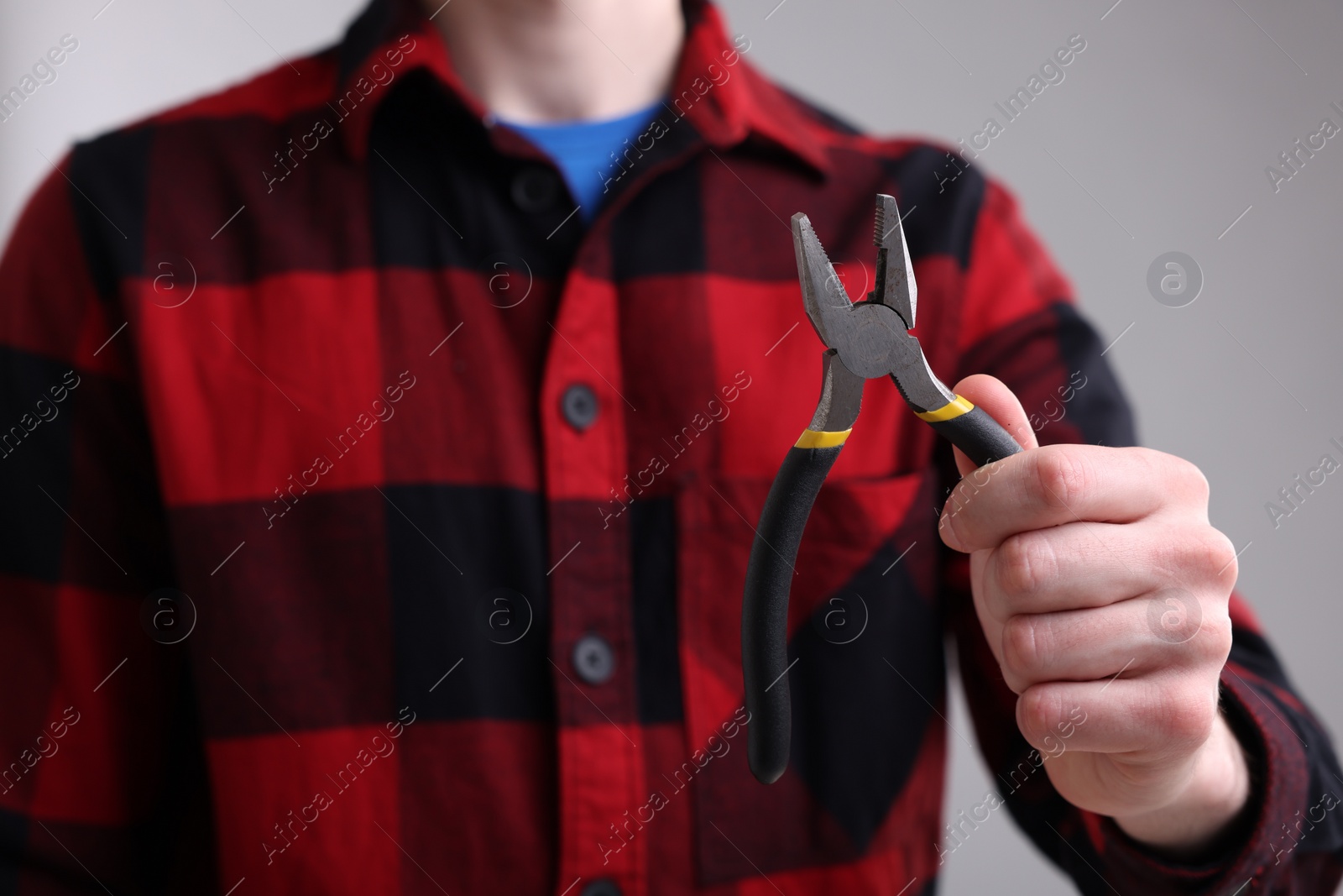 Photo of Young man holding pliers on grey background, closeup