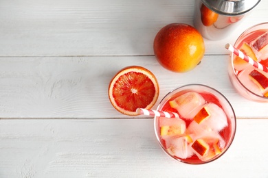 Photo of Tropical cocktail with ice cubes in glasses, fruit and shaker on wooden background, flat lay. Space for text