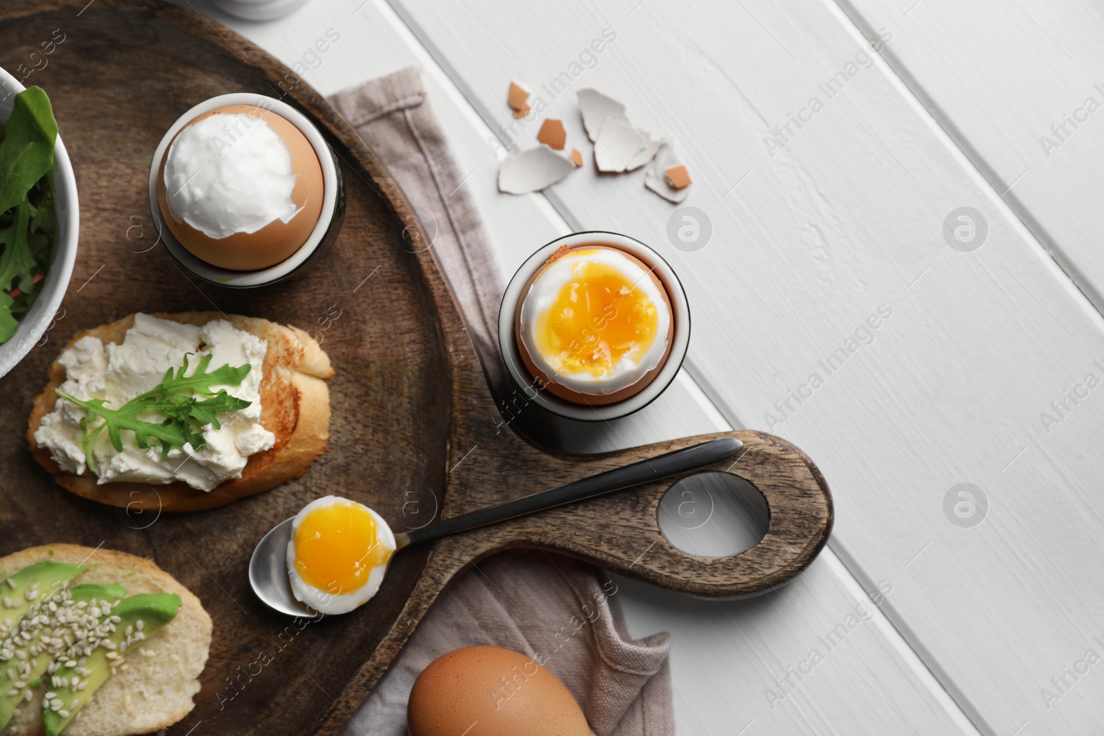 Photo of Breakfast with soft boiled eggs served on white wooden table, flat lay. Space for text