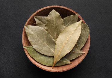 Photo of Bay leaves in wooden bowl on black background, top view