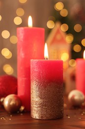 Photo of Beautiful burning candles with Christmas decor on wooden table against blurred festive lights