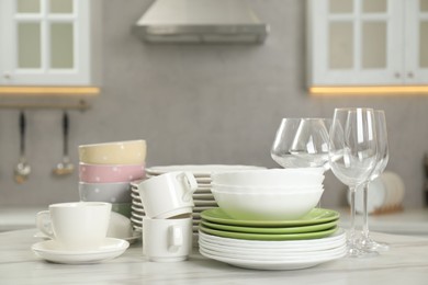 Photo of Clean plates, bowls, cups and glasses on white marble table in kitchen